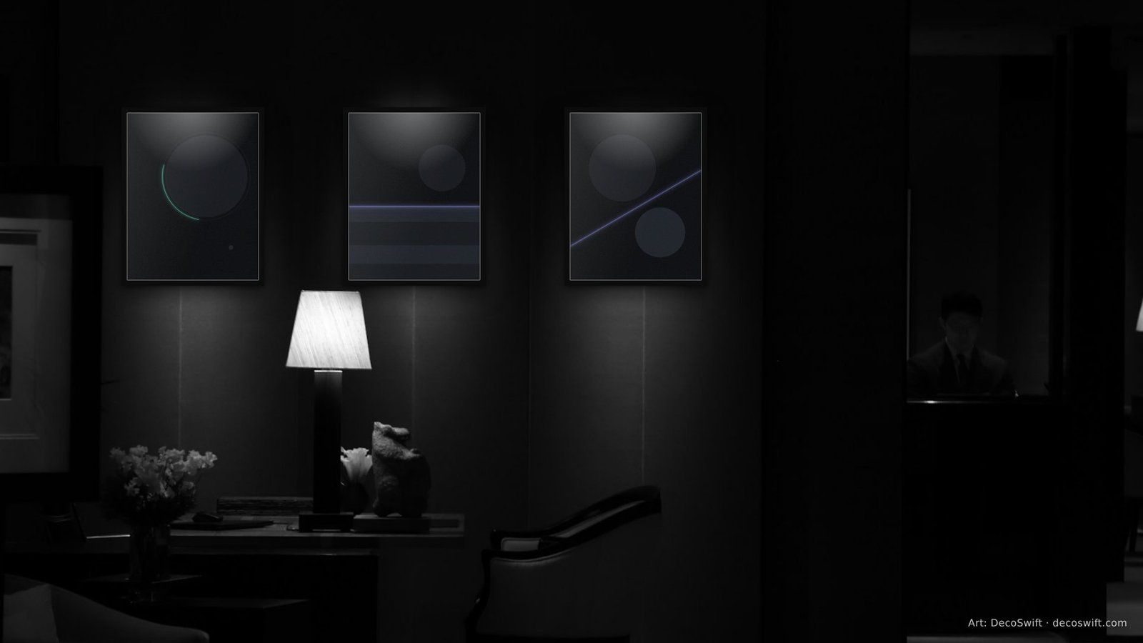 Video call background: Three Night Signal prints in slim black frames, each under its own ceiling spotlight on the dark panelled wall of a dim hotel bar, with a lit table lamp, flowers and a leather armchair below.